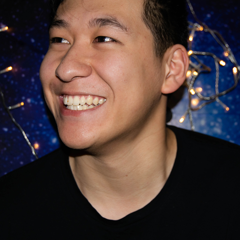 A close up photo of a man smiling at something behind the camera in front of a starry blue backdrop with LED lights.